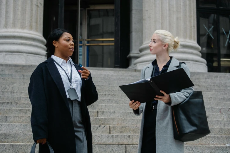 two women standing next to each other in front of a building, pexels contest winner, female lawyer, dark people discussing, charts, promotional image