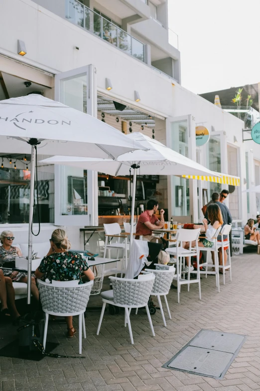 a group of people sitting at tables under umbrellas, white buildings, vancouver, oceanside, profile image