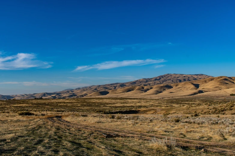 a dirt road in the middle of a field with mountains in the background, obsidian towers in the distance, clear blue skies, slide show, hillside