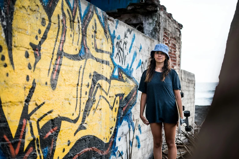 a woman standing in front of a graffiti covered wall, a portrait, pexels contest winner, yellow cap, manila, blue, thumbnail