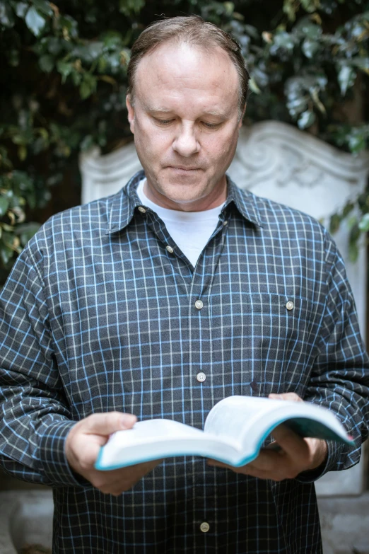 a man holding an open book in his hands, a portrait, inspired by David Simpson, unsplash, wearing a light blue shirt, rainn wilson, in garden, biblical clothing