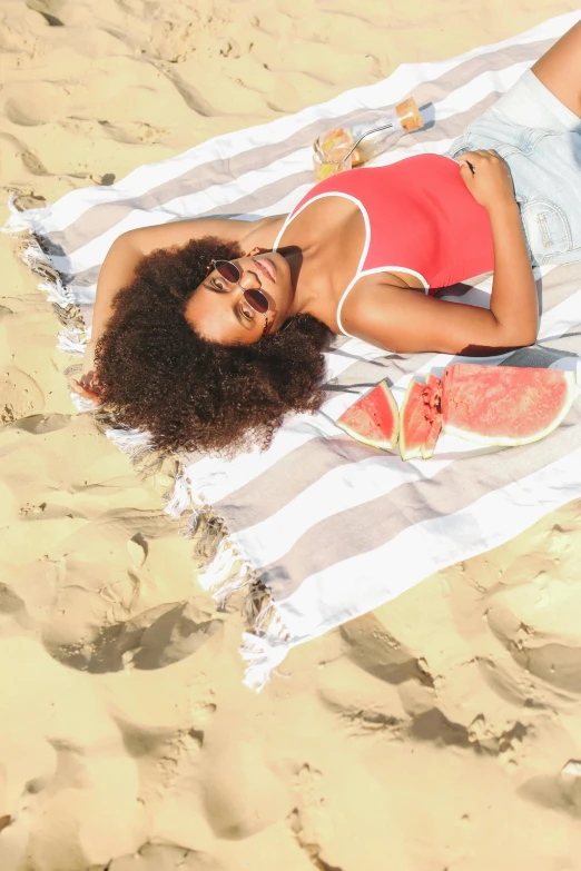 a woman laying on a towel on a beach, with afro, wavy hair spread out, shades, 2019 trending photo