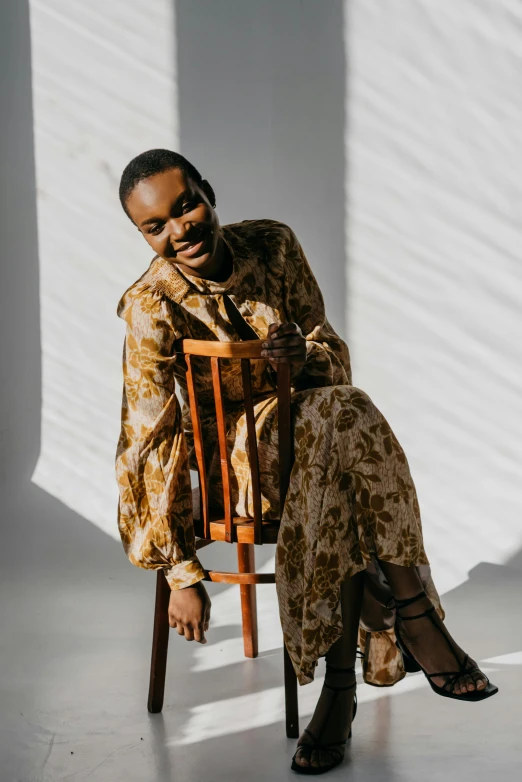 a woman sitting on top of a wooden chair, trending on pexels, baroque, wearing an african dress, laughing, muted browns, gold clothes