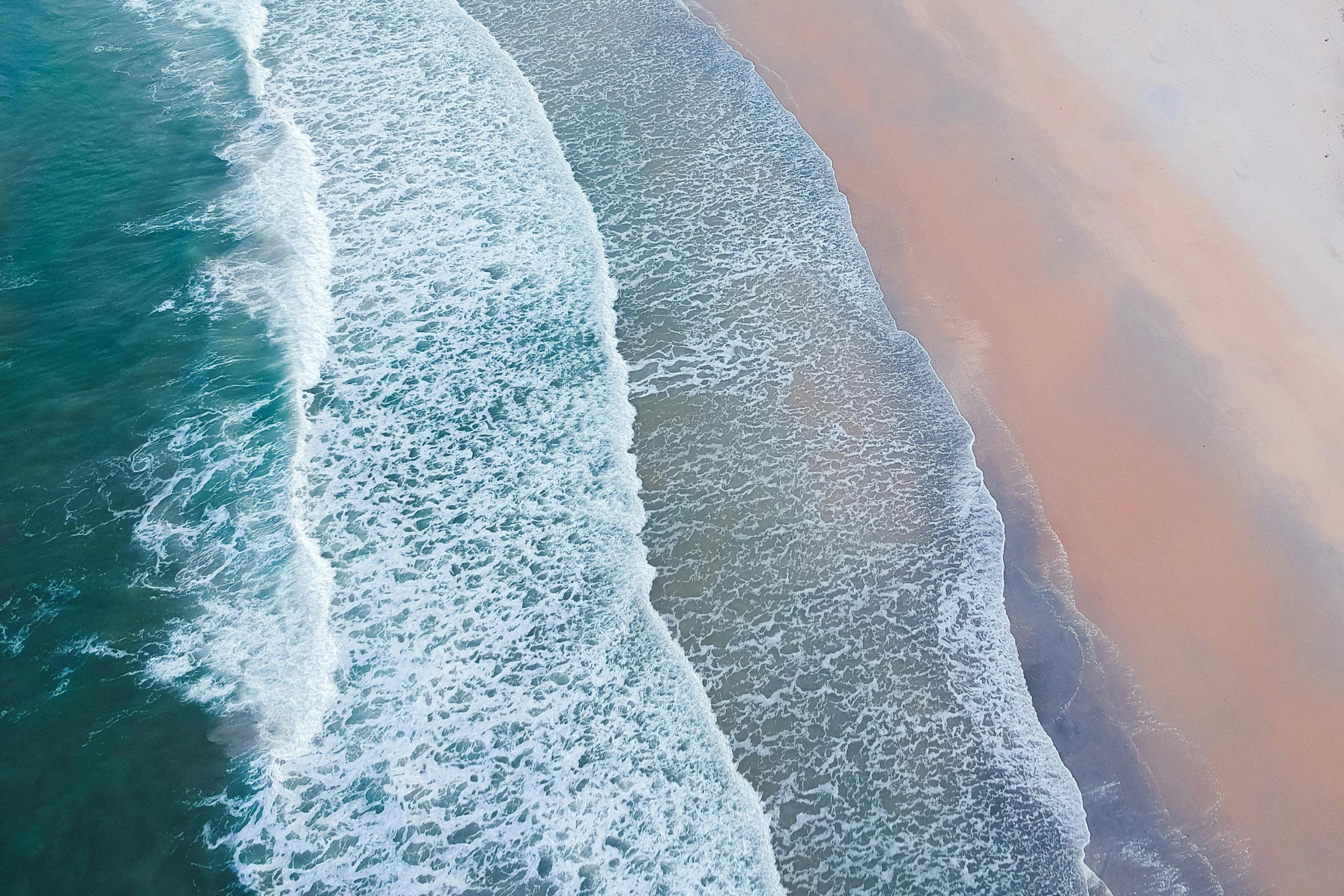 a group of people riding surfboards on top of a sandy beach, an album cover, inspired by Andreas Gursky, pexels contest winner, aerial iridecent veins, view of sea, south african coast, sea foam