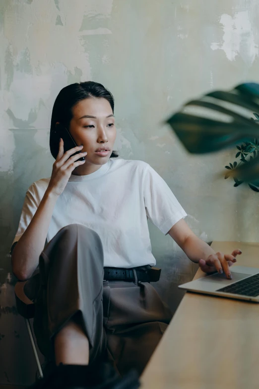 a woman sitting in front of a laptop talking on a cell phone, inspired by Ruth Jên, trending on pexels, renaissance, asian man, office clothes, dressed in a white t shirt, a lonely woman