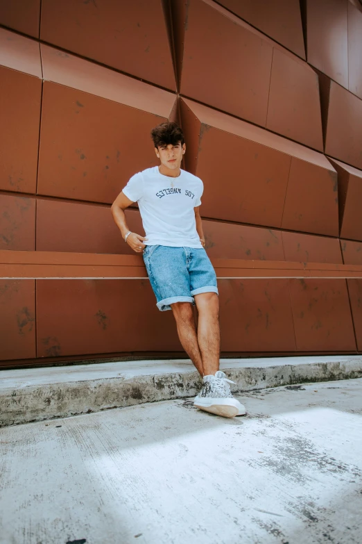 a man standing in front of a brown wall, by Cosmo Alexander, pexels contest winner, wearing shorts and t shirt, light blue and white tones, on the concrete ground, asher duran