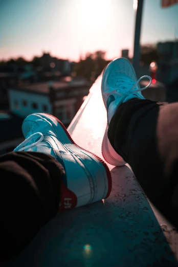 a person sitting on a ledge with their feet on a skateboard, by Niko Henrichon, trending on pexels, realism, red and white neon, white shoes, standing on rooftop, nike logo