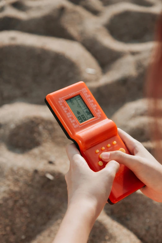 a close up of a person holding a cell phone, desert game, 80s outdoor retro arcade, terracotta, orange