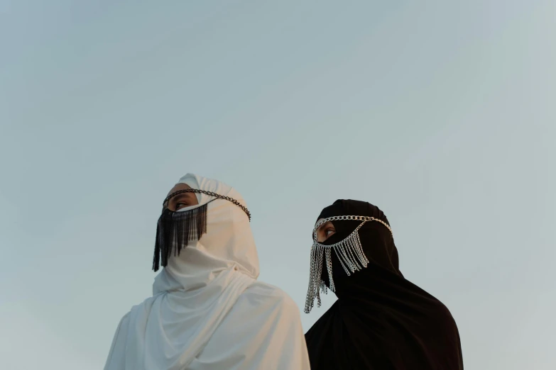 a couple of people standing next to each other, an album cover, trending on pexels, hurufiyya, his head covered in jewels, white and black clothing, arabia, minimalistic aesthetics