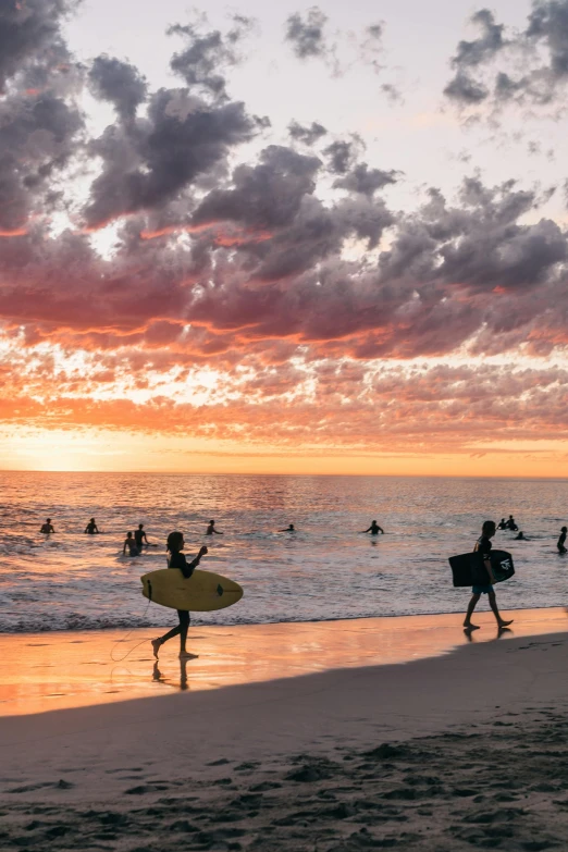 a group of people walking on top of a sandy beach, during a sunset, surfing, colorful skies, manly