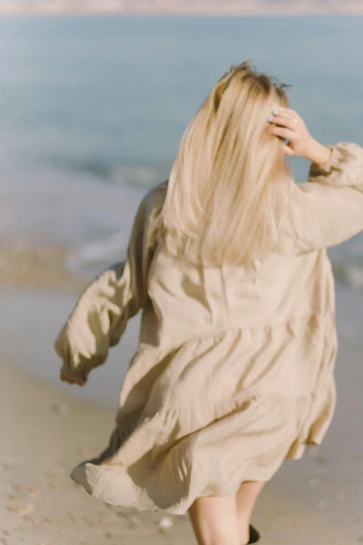 a woman walking on a beach next to the ocean, trending on pexels, renaissance, wear's beige shirt, flowing backlit hair, muted colors. ue 5, dirty linen robes