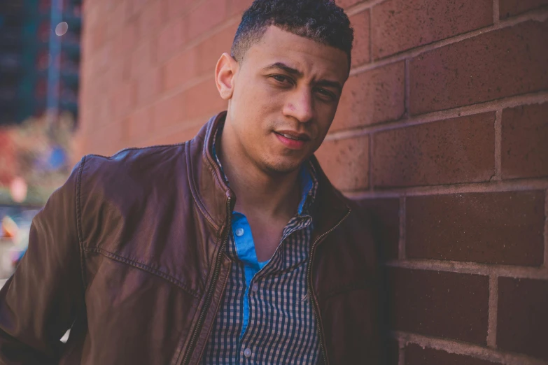 a young man leaning against a brick wall, an album cover, inspired by Carlos Berlanga, light brown skin, portrait image