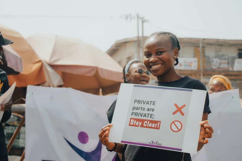 a woman holding a sign in front of a crowd, pexels, private press, avatar image, light skinned african young girl, clean environment, wearing translucent sheet