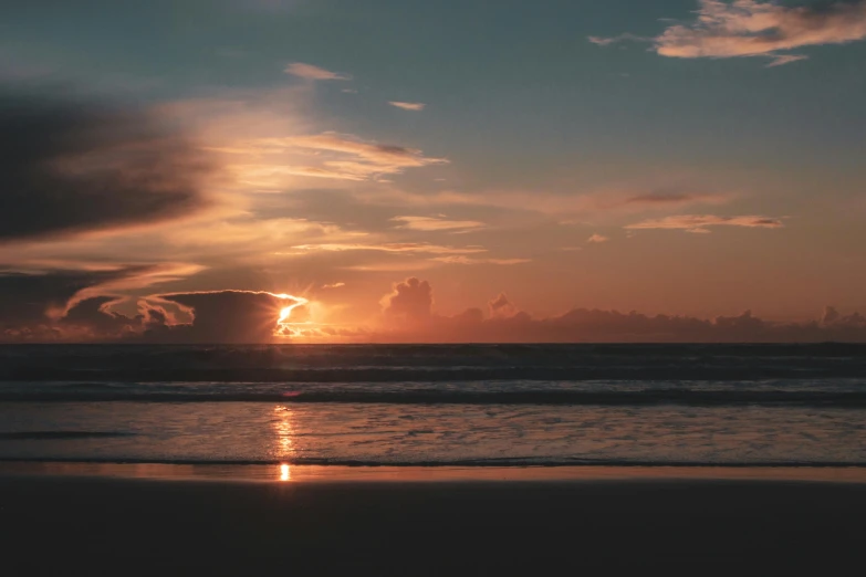 the sun is setting over the ocean on the beach, unsplash contest winner, gold coast australia, night time low light, burning clouds, slightly tanned