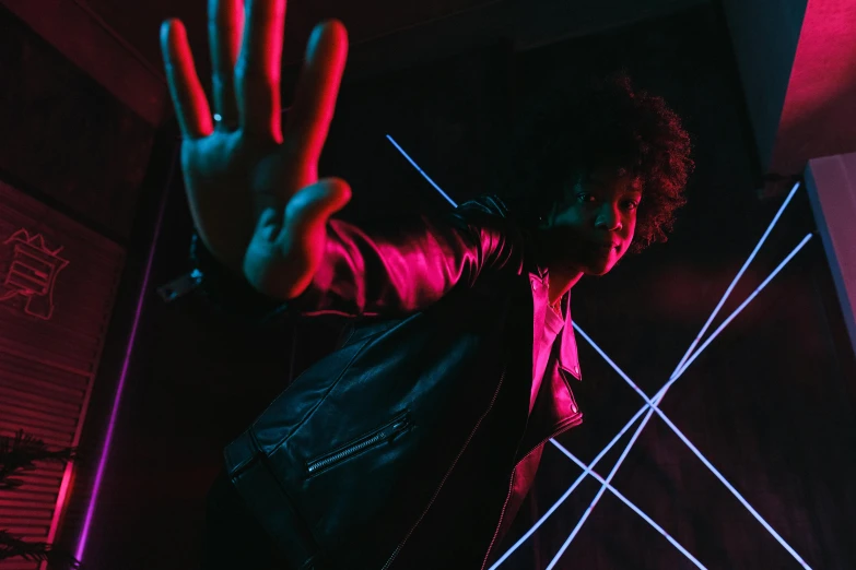 a man standing in front of a neon light, an album cover, pexels, threatening pose, afro tech, leather clothes, light room