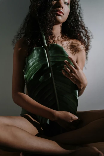 a woman in a green dress sitting on a bed, an album cover, inspired by Elsa Bleda, trending on pexels, big leaf bra, exotic flora, 🍸🍋, dark-skinned