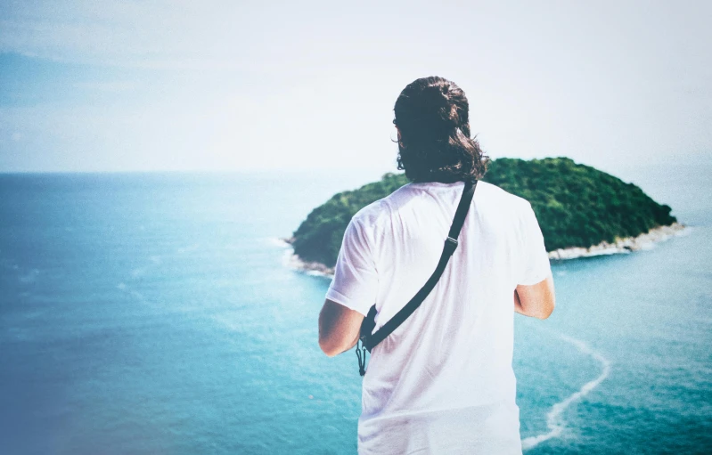 a man standing on top of a cliff overlooking a body of water, pexels contest winner, man in white t - shirt, over his shoulder, chillwave, retro effect