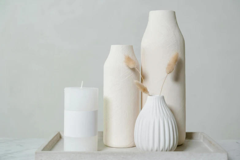 a white vase sitting on top of a table next to a candle, minimalism, bottles covered in wax, detailed product image, matte accents, pastel'