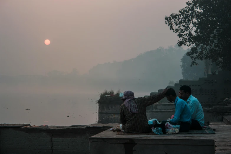 a couple of people sitting on a bench next to a body of water, pexels contest winner, nepal, hazy sun and mystical, people at work, low light