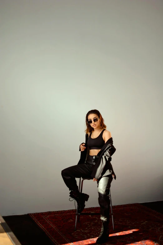 a woman sitting on a chair with a gun in her hand, inspired by Zhu Da, trending on pexels, minimalism, dressed in biker leather, wearing a crop top, with sunglass, full body photgraph