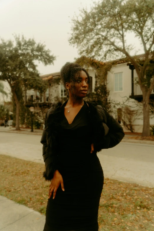 a woman in a black dress standing on a sidewalk, by Winona Nelson, sza, young southern woman, high quality image, multiple stories
