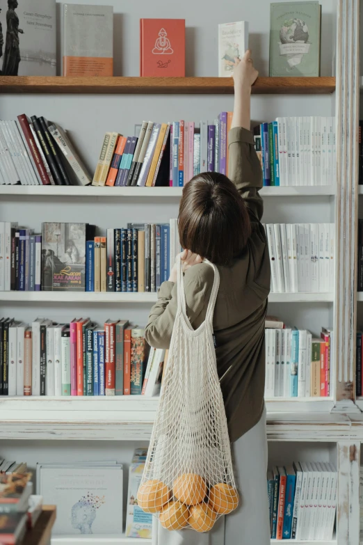 a little girl that is standing in front of a book shelf, holding mesh bag with bagels, cottagecore hippie, raising an arm, 2019 trending photo