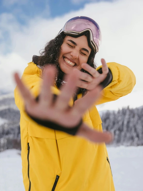 a woman standing on top of a snow covered slope, a picture, pexels contest winner, wearing a yellow hoodie, wave a hand at the camera, taking control while smiling, avatar image
