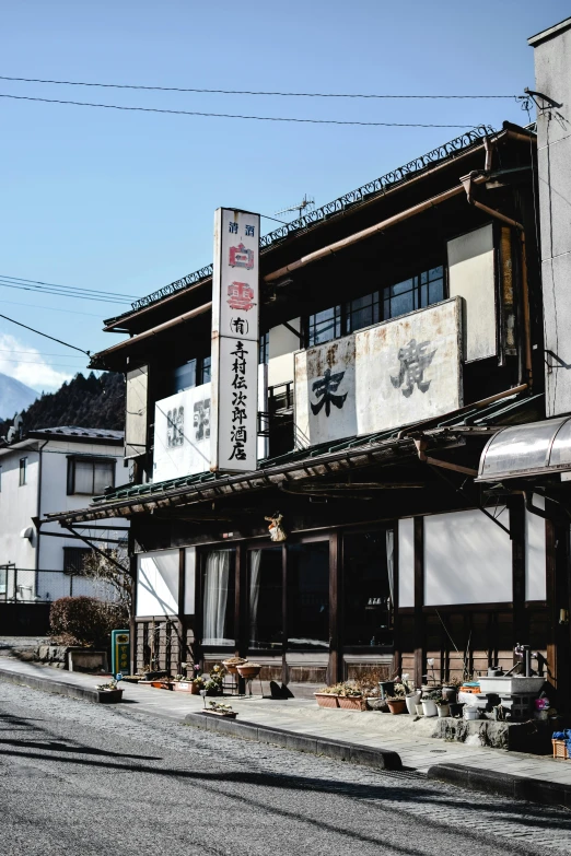a couple of buildings sitting on the side of a road, shin hanga, restaurant, with mountains in background, with white kanji insignias, trending photo