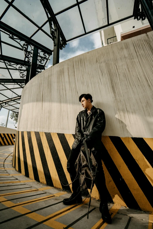 a man in a leather jacket leaning against a wall, an album cover, inspired by Zhang Han, unsplash, overpass, black and yellow, pentagon, on ship