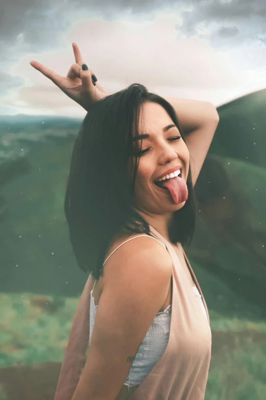 a woman standing on top of a lush green hillside, trending on pexels, happening, licking tongue, brunette woman, winking at the camera, brandon woelfel