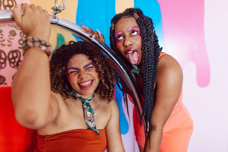 two women posing for a picture in front of a mirror, trending on pexels, afrofuturism, with a tentacle - shaped tongue, muted rainbow tubing, revellers, laughing your head off