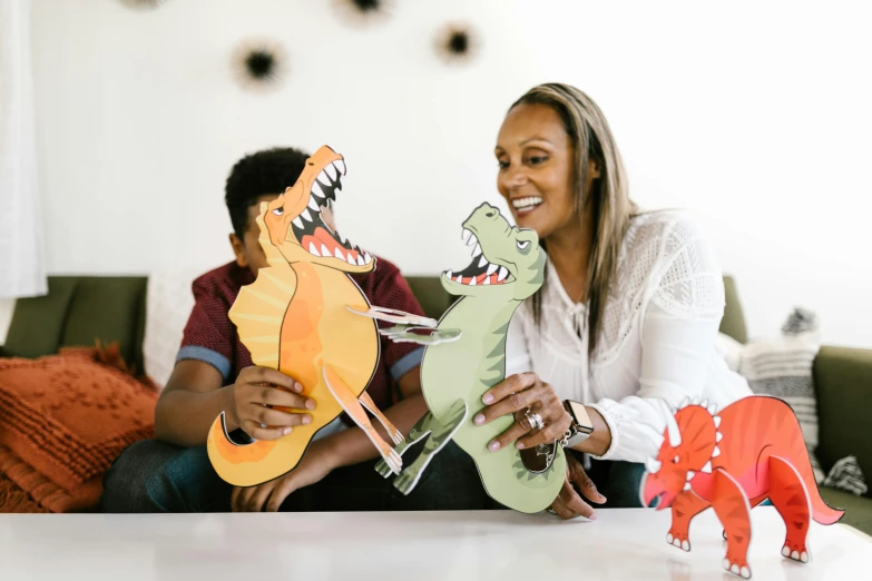 a woman sitting on a couch holding two paper dinosaurs, a cartoon, by Lee Loughridge, pexels contest winner, interactive art, families playing, made of cardboard, husband wife and son, riyahd cassiem