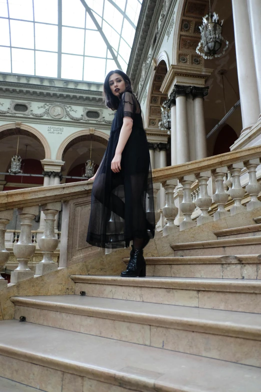a woman standing on the steps of a building, inspired by Elsa Bleda, pexels contest winner, baroque, gothic girl dressed in black, dua lipa, on the altar, androgynous person