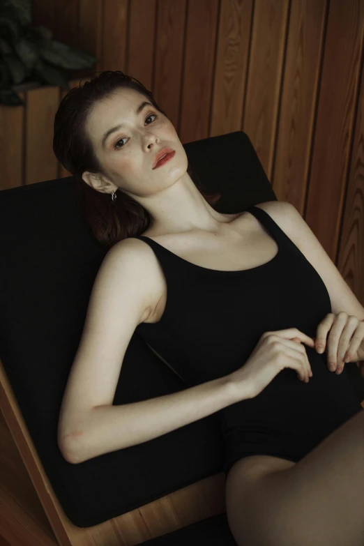 a woman in a black dress sitting in a chair, inspired by Elsa Bleda, reddit, wearing tanktop, natural soft pale skin, kiko mizuhara, skintight black bodysuit