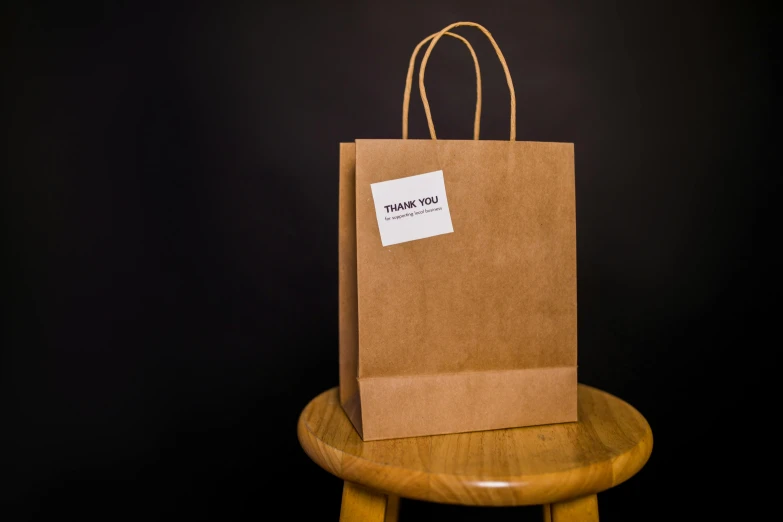 a brown paper bag sitting on top of a wooden stool, presenting wares, thank you, detailed product image, front facing shot