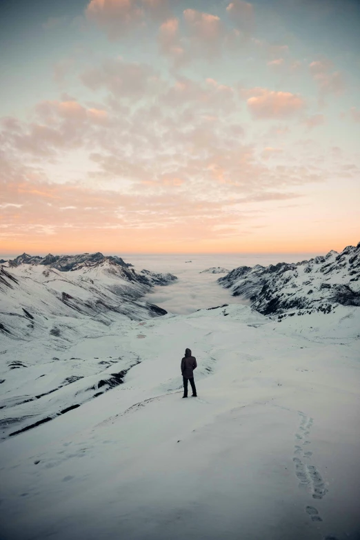 a man standing on top of a snow covered slope, an album cover, inspired by Werner Andermatt, pexels contest winner, sunset view, andes, expansive cinematic view, looking down from above