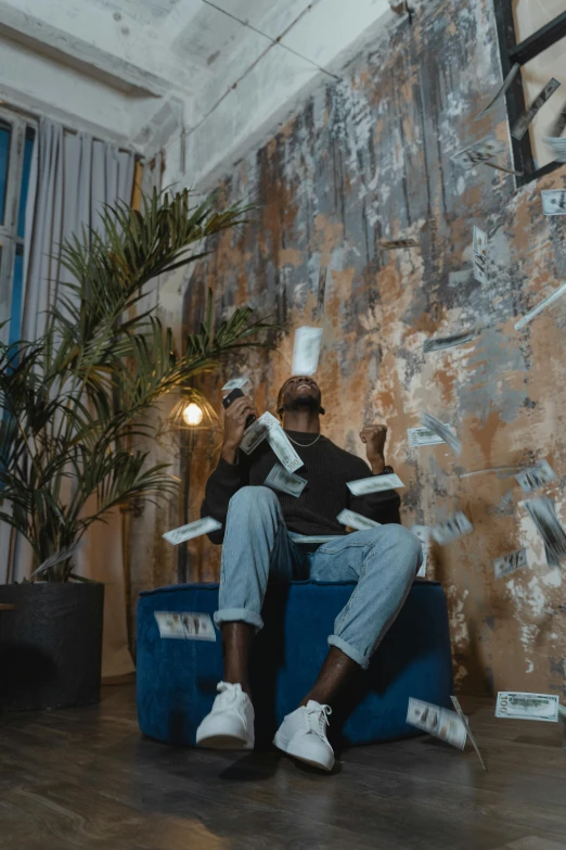 a man sitting on a blue chair in a room, an album cover, by artist, pexels contest winner, visual art, banknotes flying from barrel, virgil abloh, video footage, ( ( theatrical ) )