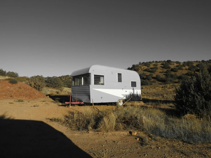 a trailer parked on the side of a dirt road, a portrait, by Lee Loughridge, unsplash, retrofuturism, caravan, hillside, opal, gray