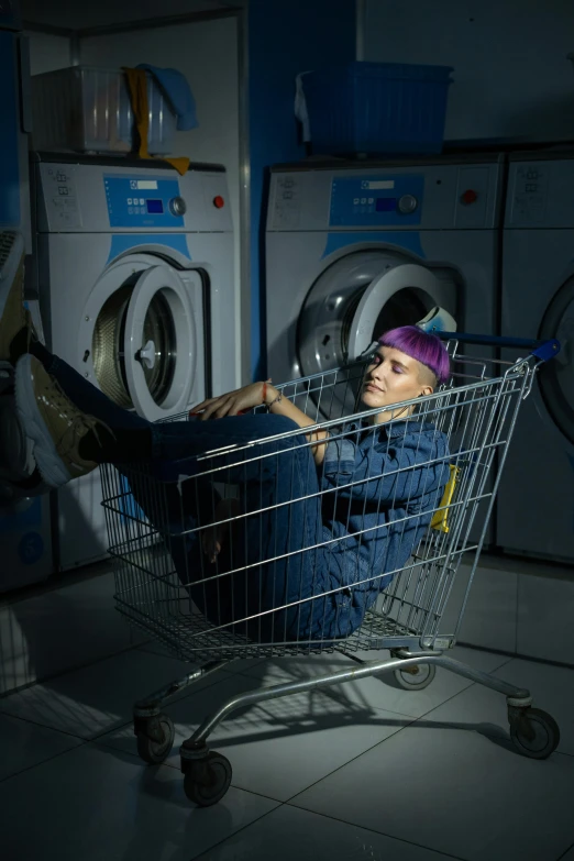 a man sitting in a shopping cart in a laundry room, an album cover, inspired by Elsa Bleda, pexels contest winner, renaissance, die antwoord, work clothes, non-binary, mechanic