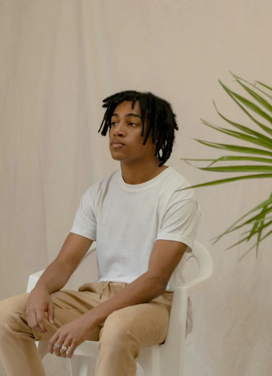 a man sitting on a chair next to a potted plant, an album cover, inspired by Xanthus Russell Smith, trending on unsplash, white tshirt, portrait willow smith, frank dillane, profile image