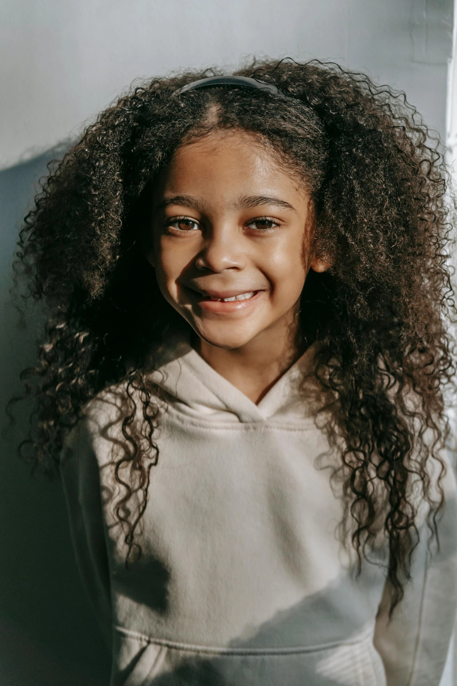 a young girl with curly hair posing for a picture, wearing a hoodie, light brown skin, diverse haircuts, with textured hair and skin