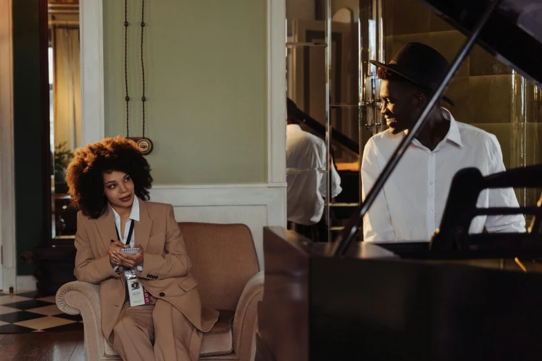 a woman sitting on a couch next to a piano, by Emma Andijewska, pexels contest winner, with afro, man and woman, hotel room, in a meeting room