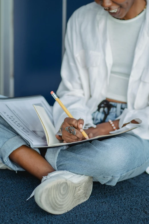 a man sitting on the floor writing on a piece of paper, pexels contest winner, academic art, african american young woman, white shirt and blue jeans, holding pencil, holding spell book