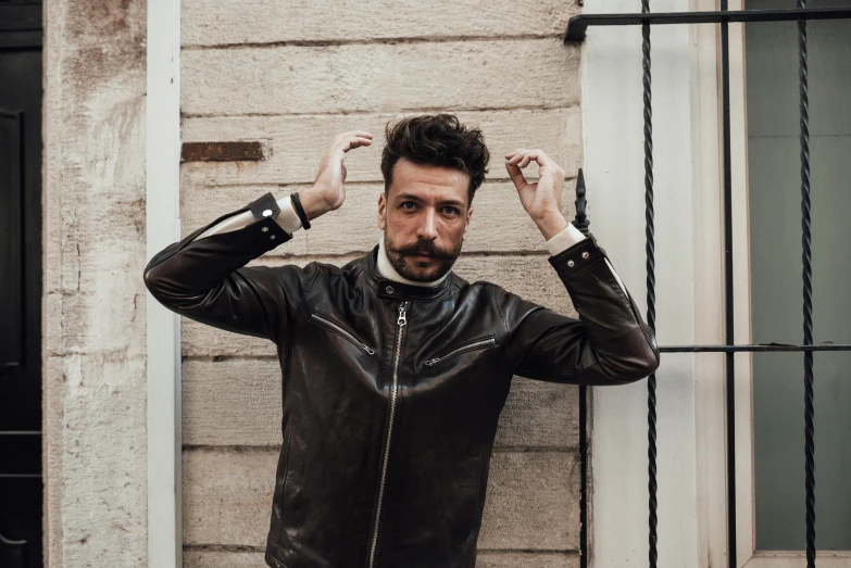 a man in a leather jacket leaning against a wall, inspired by Francesco Furini, pexels contest winner, renaissance, beard stubble, square masculine jaw, triumphant pose, cafe racer