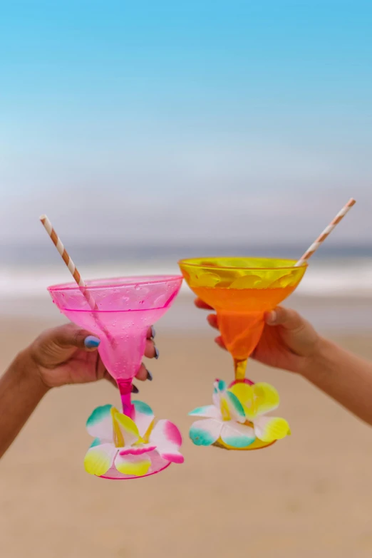 two people holding up cocktail glasses on the beach, multicoloured, crafts, parties, flatlay