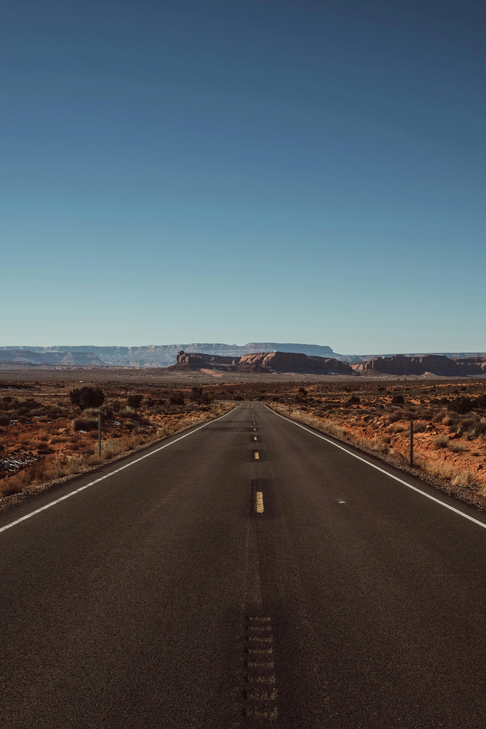 an empty road in the middle of the desert, unsplash, clear blue skies, moab, giant crater in distance, background image
