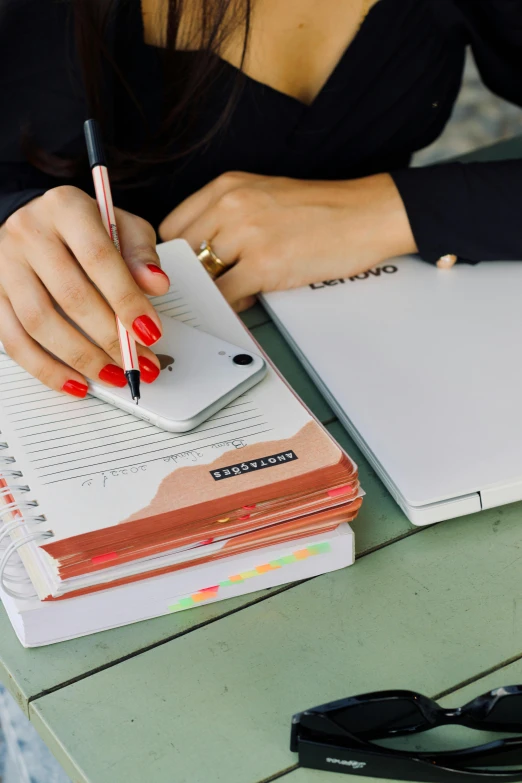 a woman sitting at a table writing on a notebook, trending on pexels, white and red color scheme, holding a stack of books, taking from above, rounded corners