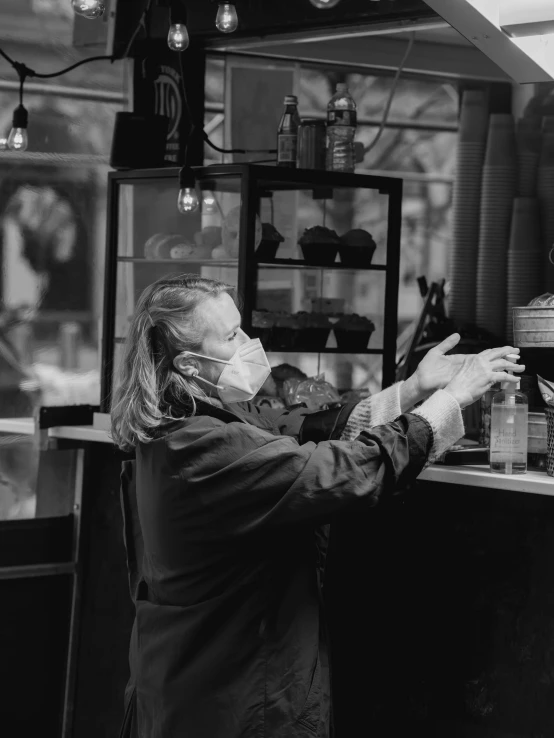 a black and white photo of a woman in a kitchen, process art, in a bright cafe, old man doing with mask, covid, medium format. soft light