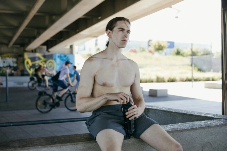 a shirtless man sitting on top of a cement bench, pexels contest winner, wearing black shorts, bicycle in background, avatar image, he is about 20 years old | short