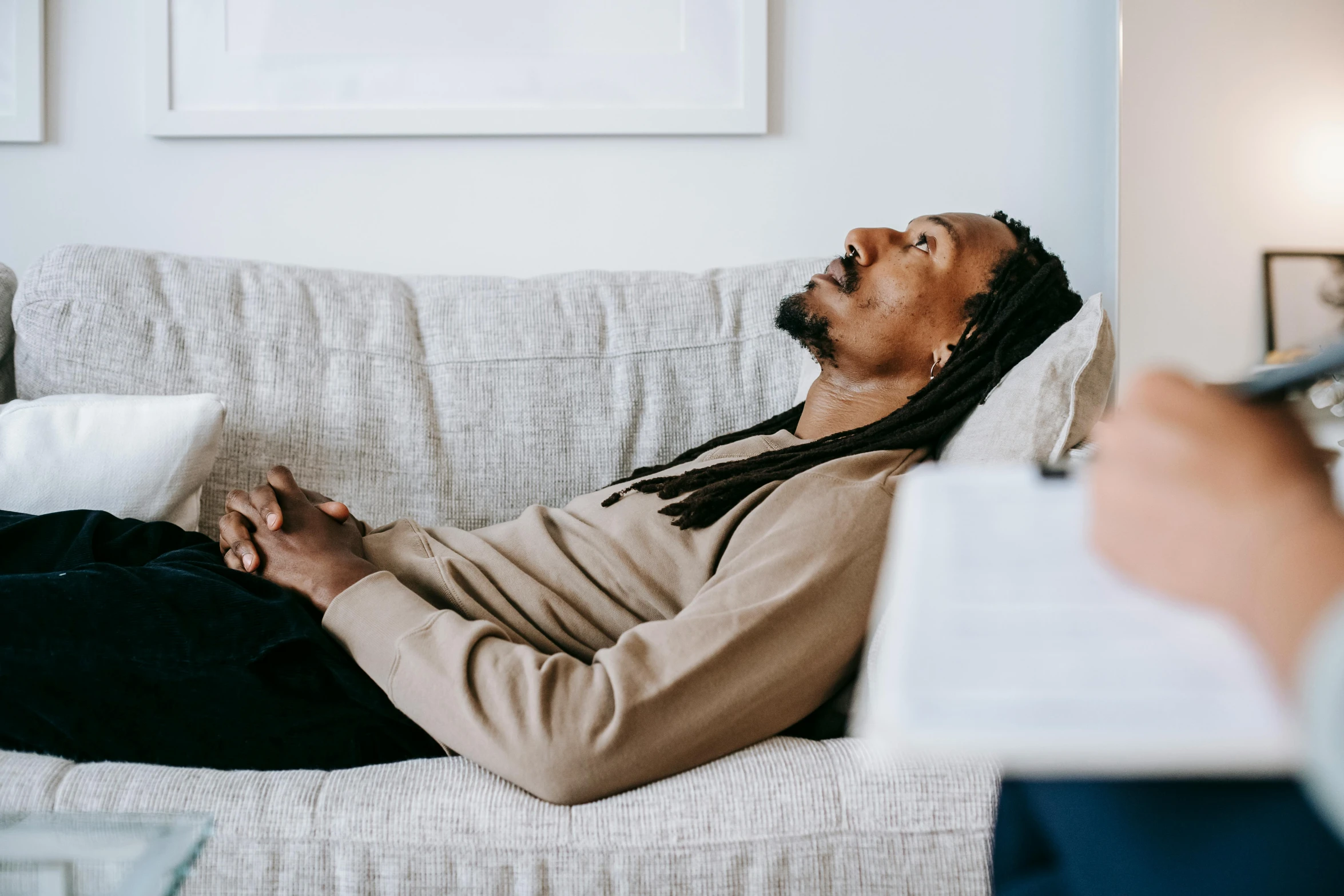 a man with dreadlocks laying on a couch, by Everett Warner, trending on pexels, acupuncture treatment, calmly conversing 8k, black jesus, facing sideways